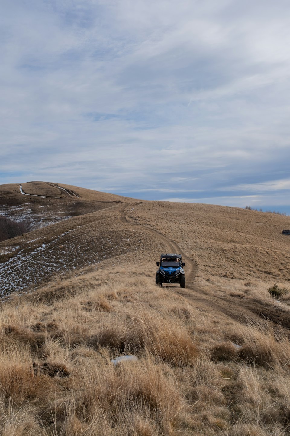 Blue utility terrain vehicle on a winding dirt track through rolling hills.