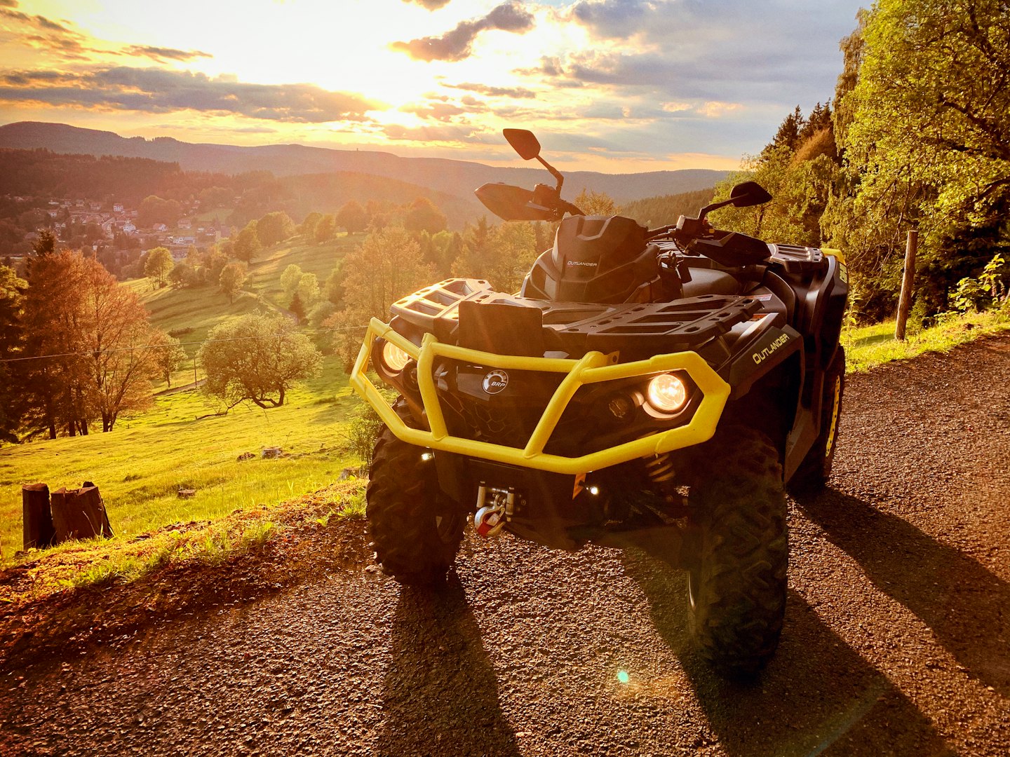 Black and yellow ATV parked on a gravel path overlooking hills.