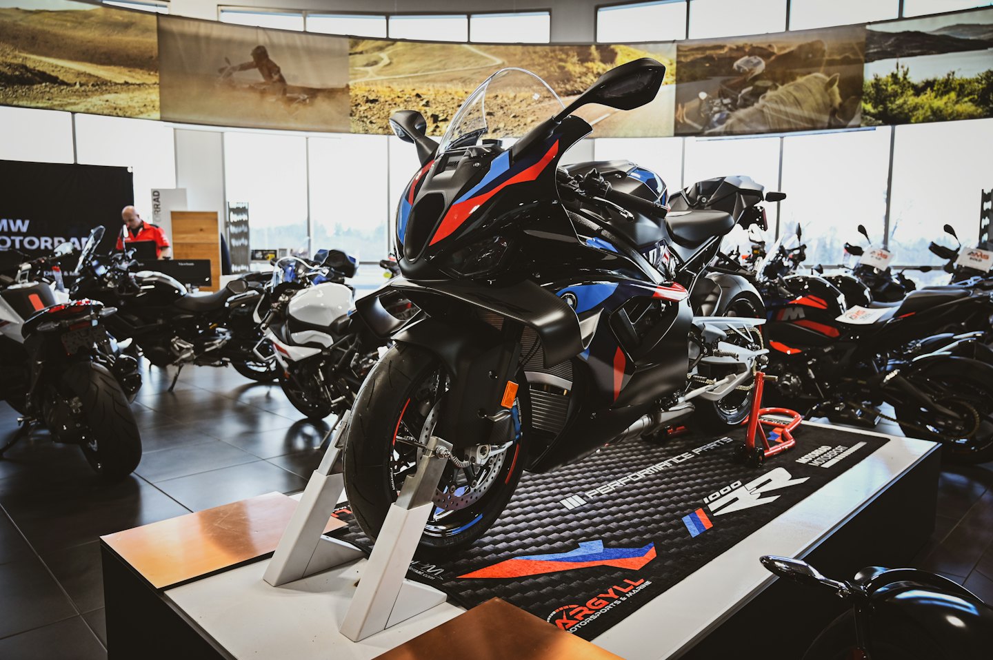 A modern motorcycle sits on a stand in a dealership showroom.