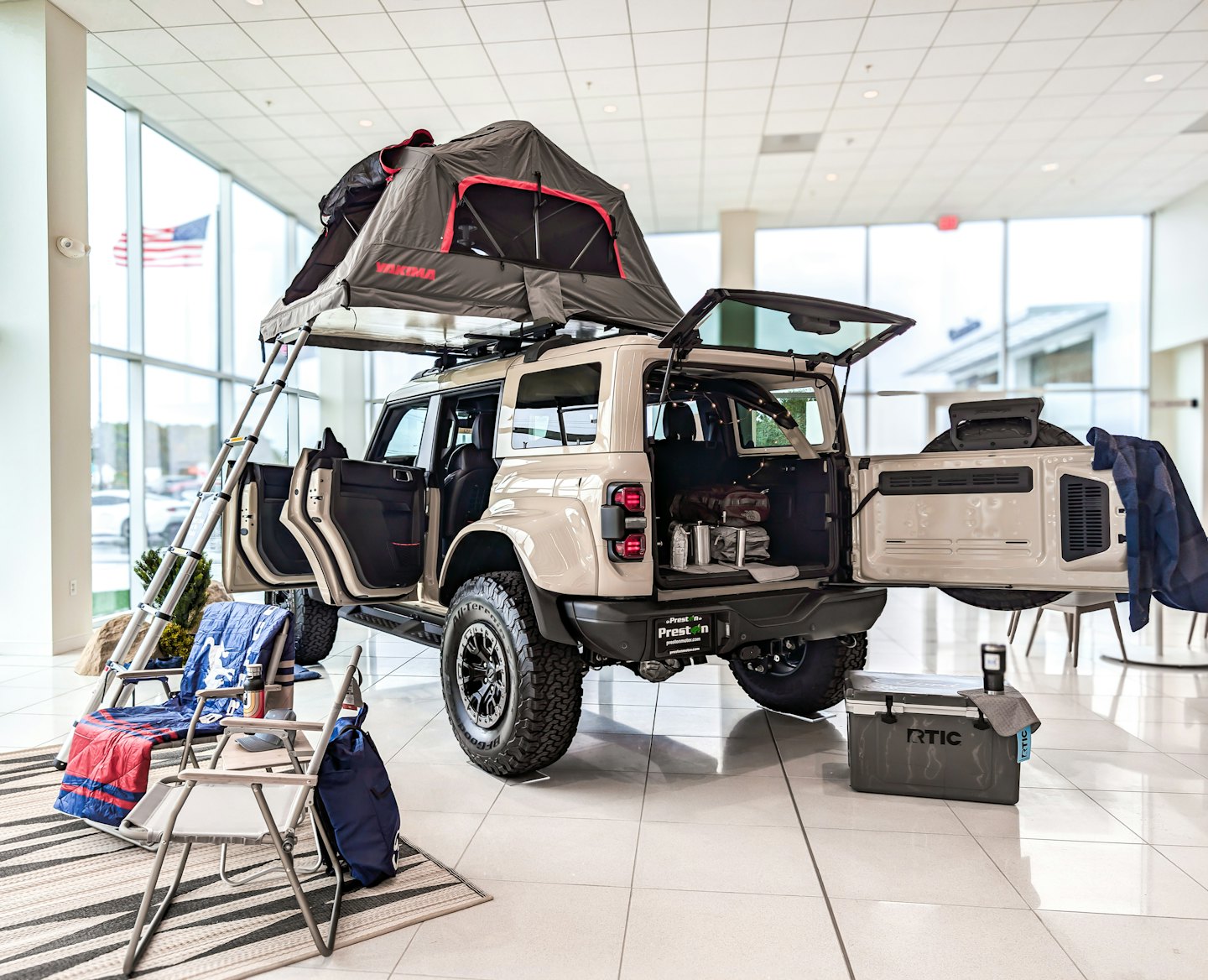 Off-road SUV with rooftop tent and camping gear in showroom.